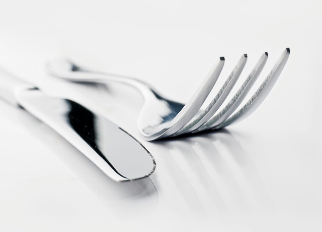 Blank gaffel, kniv og ske på lys baggrund