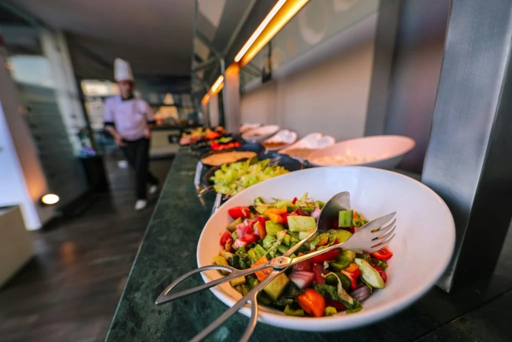 Hvid skål med salat og serveringsbestik på en buffet