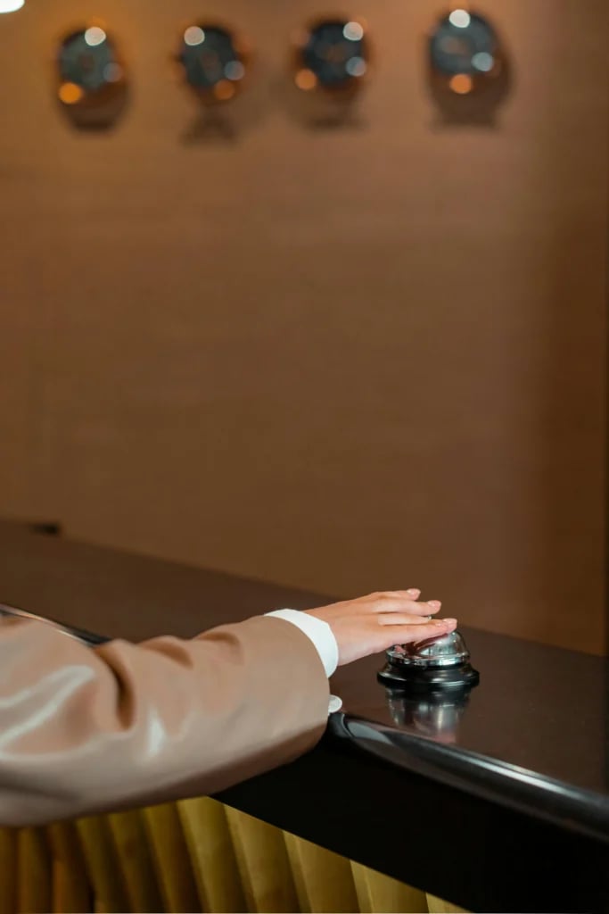 Hånd trykker på en receptionsklokke på en mørk disk