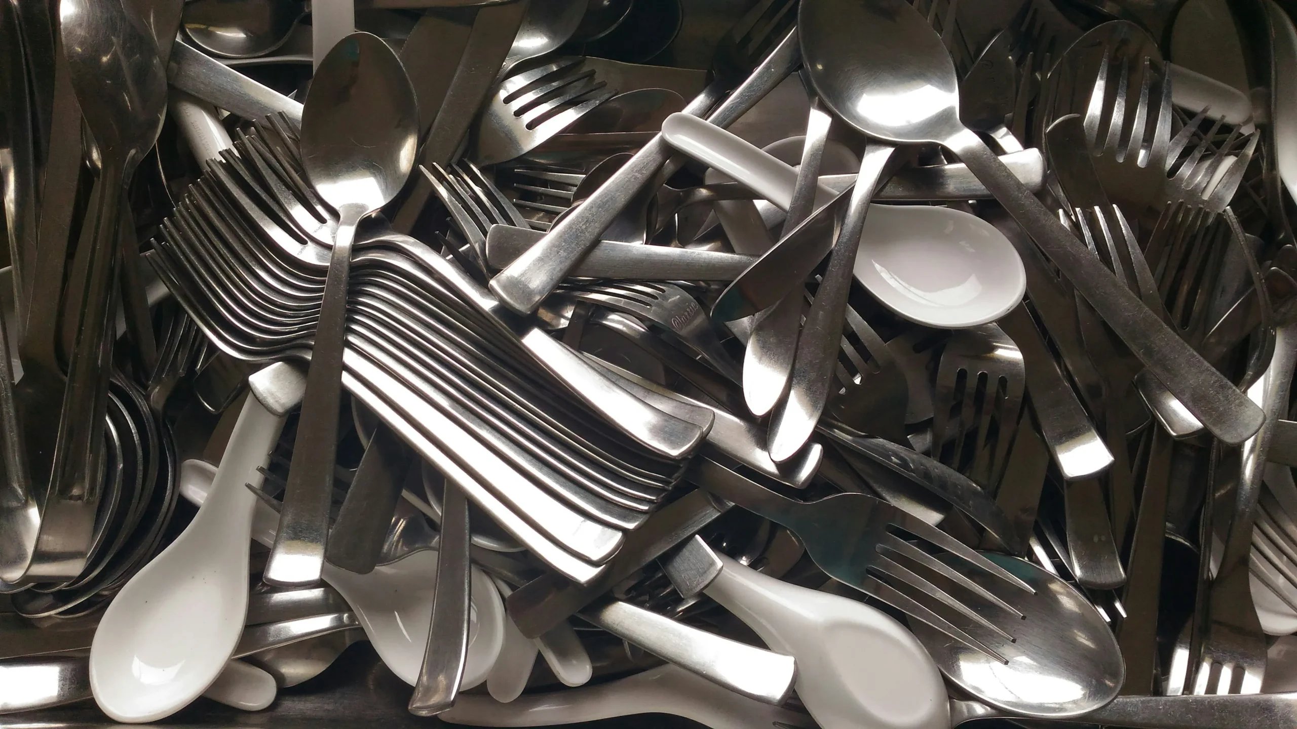 En bunke gafler, knive og skeer i metal sammen med hvide skeer
