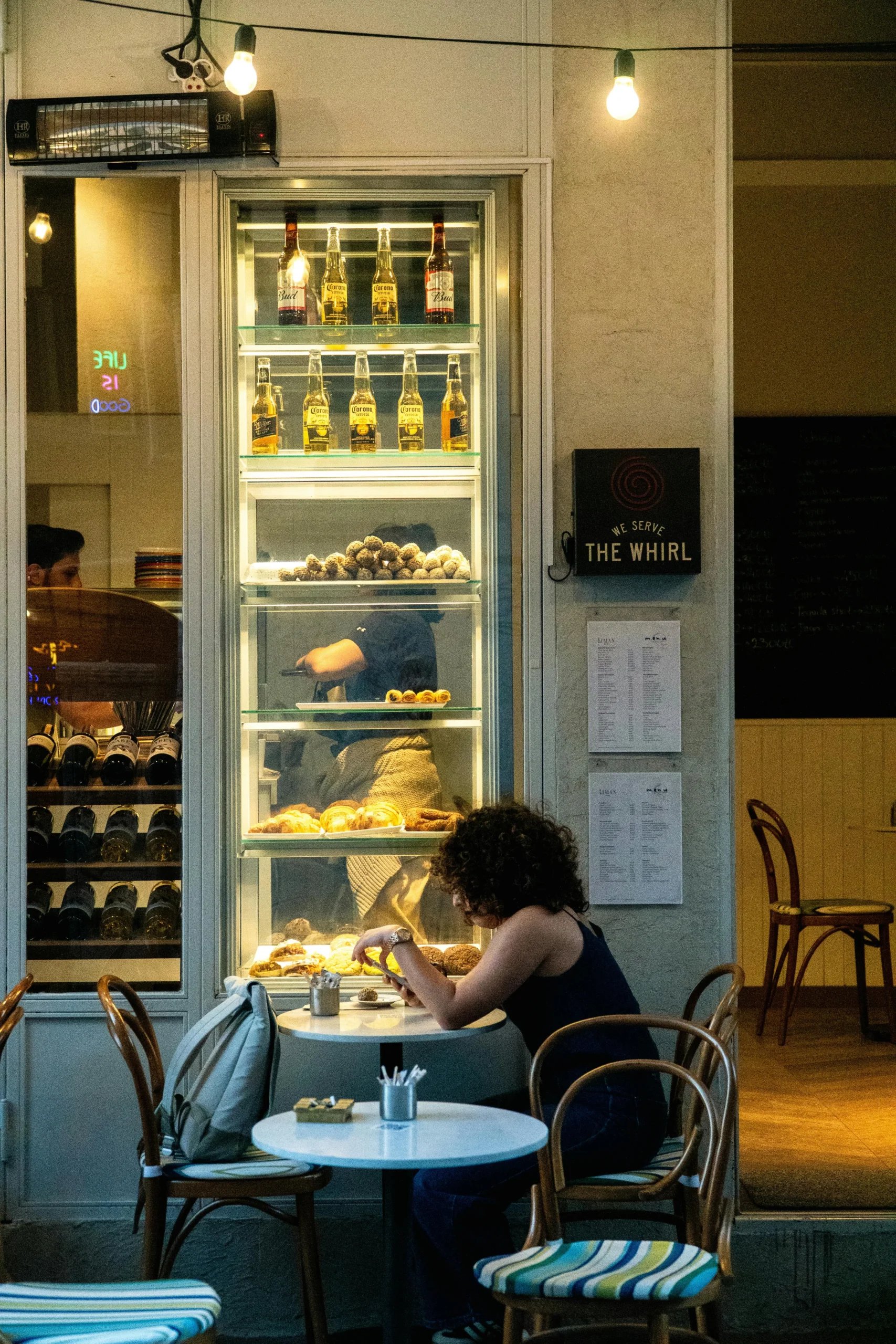 Oplyst kølemontre med flasker og mad ved små caféborde