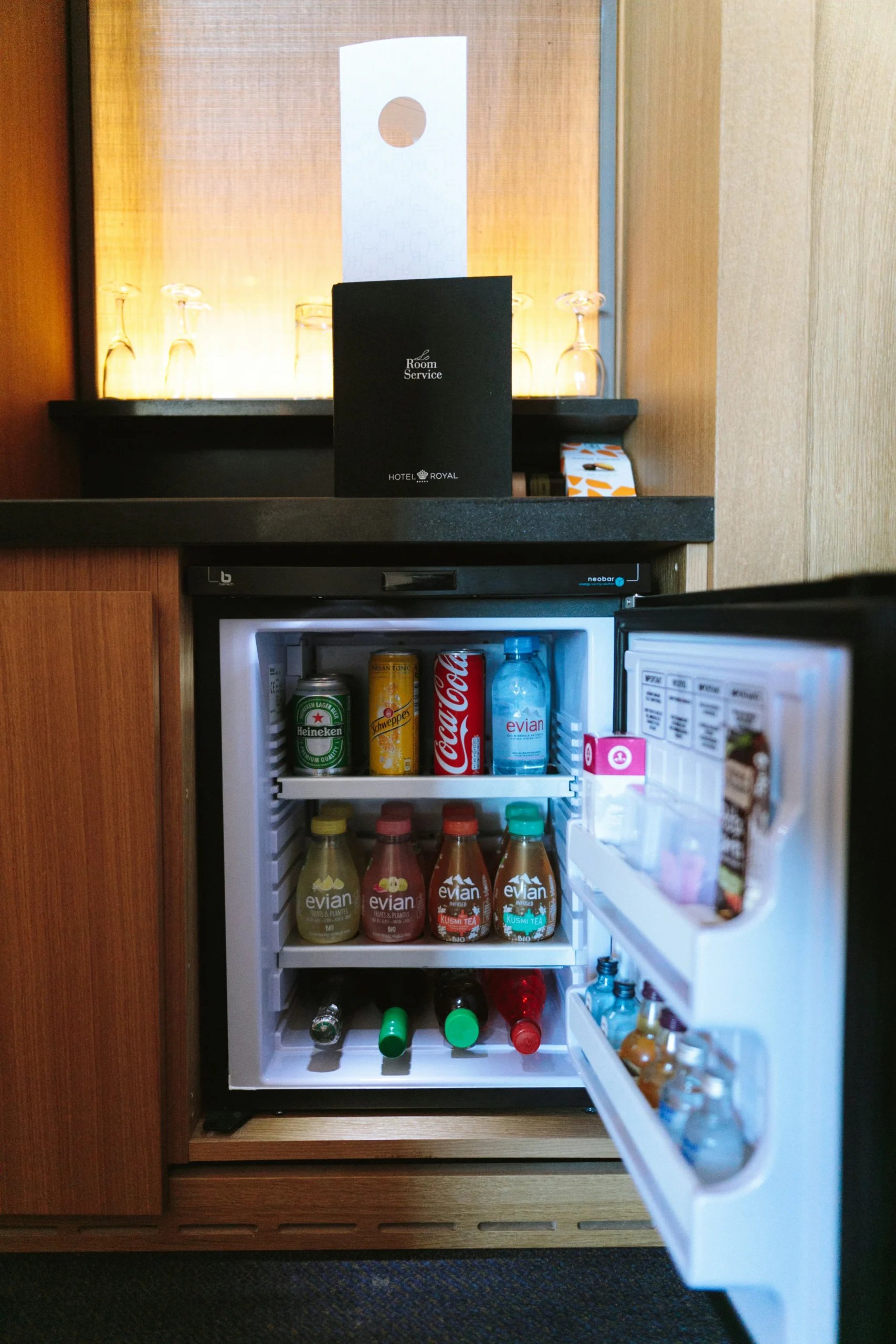 Åben minibar med flasker og dåser i et træmøbel