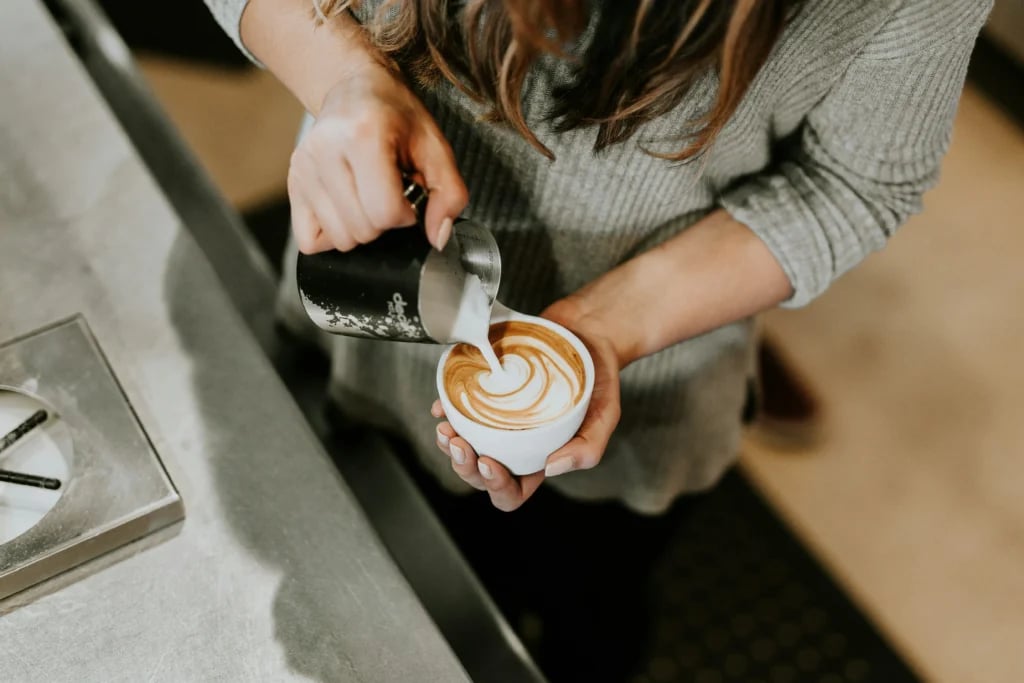 Barista hælder mælk i kaffe og laver latte art