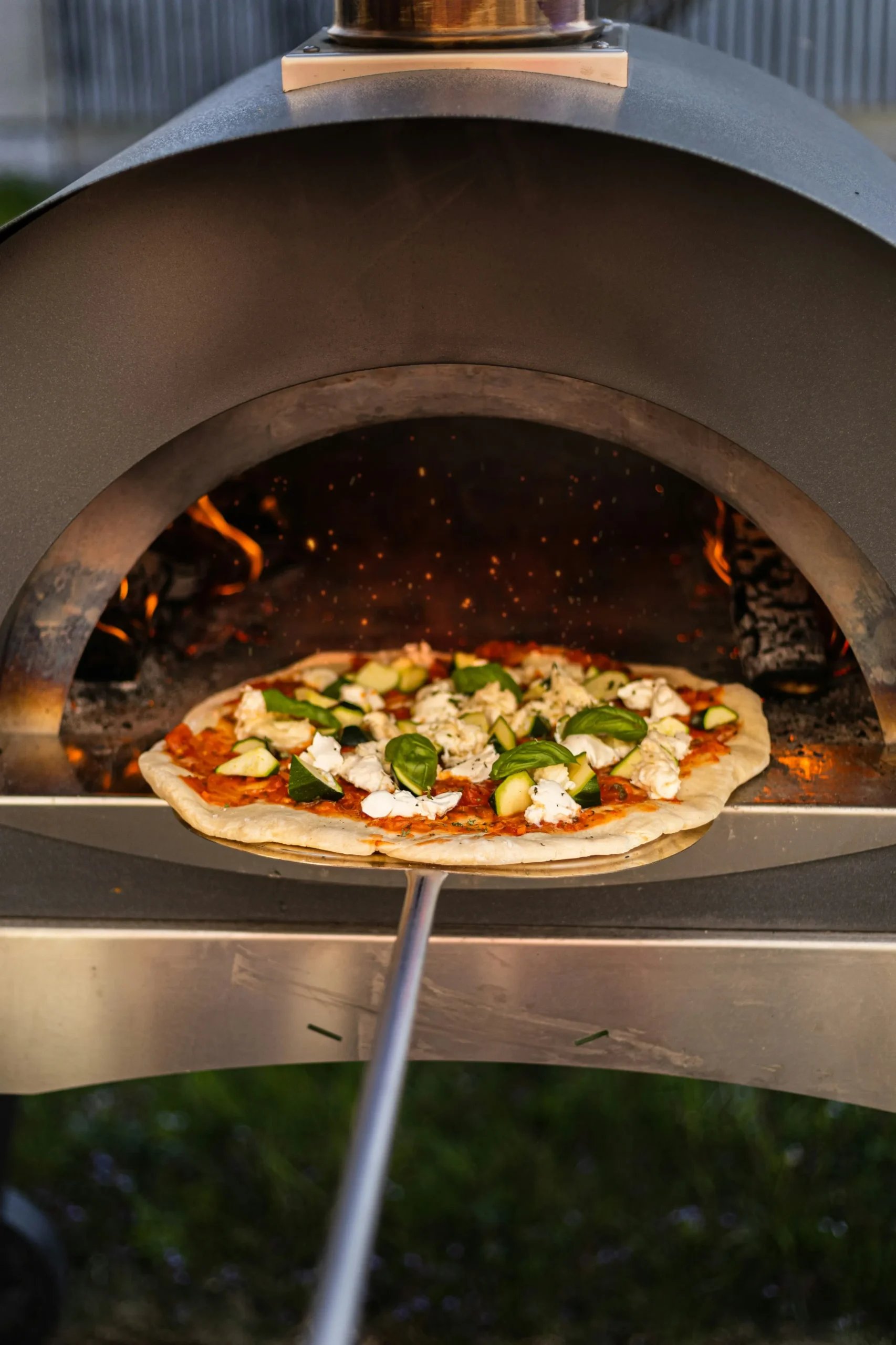 Pizza på en pizzaspade foran en ovn med ild i baggrunden